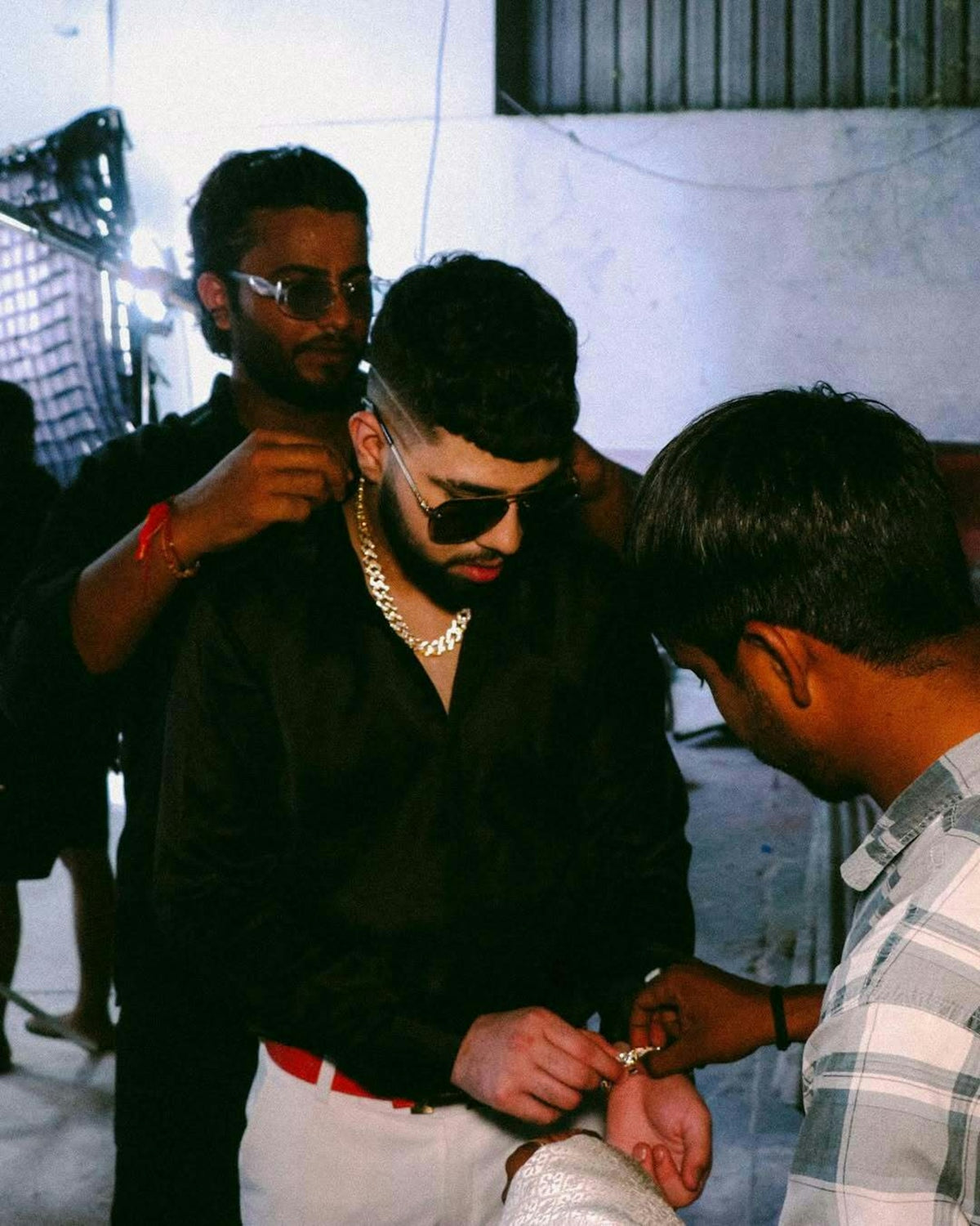 Men dressing a man in a black shirt and jewelry